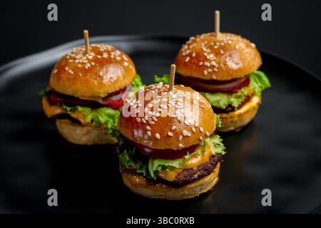 Trois mini cheeseburgers juteux sur fond noir. Banque D'Images