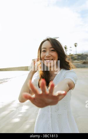 Une femme sourit et ouvre la main vers la caméra à la plage, prise de vue verticale. Banque D'Images