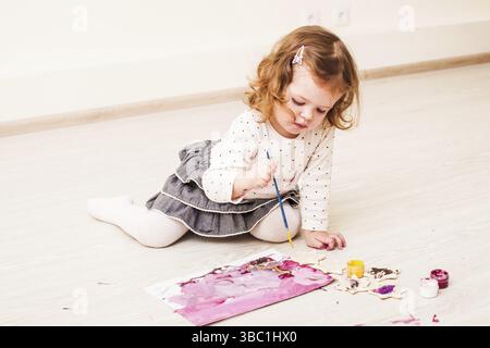 Fille, c'est peindre avec un pinceau et gouache sur papier sur le plancher Banque D'Images