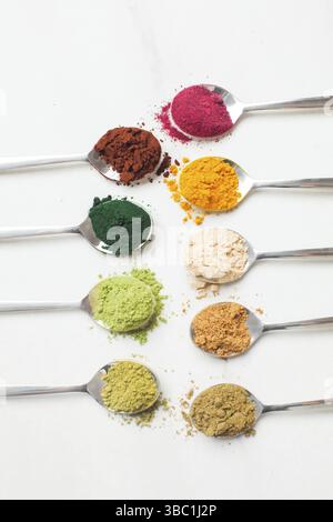 Différents types de poudres superalimentaires colorées dans des cuillères. Vue de dessus des boosters Smootie sains sur la table blanche Banque D'Images
