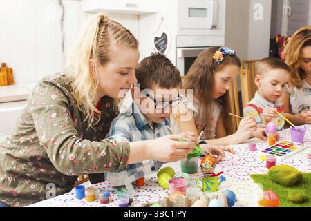 Jeunes femmes enfants heping créant un décor printanier pour Pâques. Mère et son fils tenant des pinceaux de peinture de l'oeuf coloré Banque D'Images