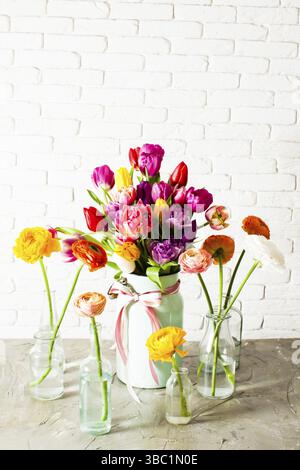 Adorable bouquet multicolore fait de tulipes gaies et lumineuses, mis en boîte métallique. Plusieurs bouteilles en verre avec des fleurs ranunculus debout autour. Blanc b Banque D'Images