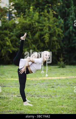 Mère sportive et fille s'étirant sur l'herbe dans un parc, fille s'étendant sur le dos de la mère Banque D'Images