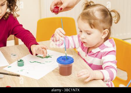 Fille, c'est peindre avec un pinceau et d'aquarelles sur papier dans le jardin d'enfants Banque D'Images
