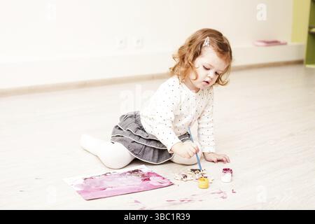 Fille, c'est peindre avec un pinceau et gouache sur papier sur le plancher Banque D'Images