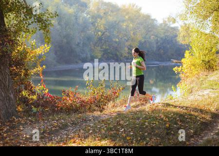 Slimfit Active formation femme à l'automne parc de la ville, près de la rivière. Femme avec bonne hygiène de vie fait son concept de routine en cours à l'automne cit Banque D'Images