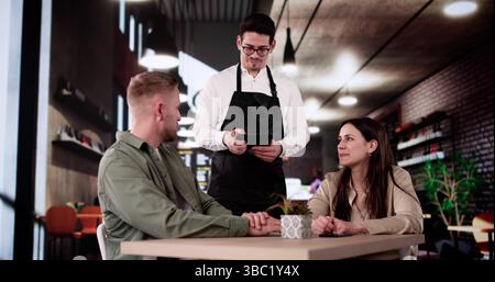 Serveur romantique prenant le dîner commande d'un couple élégant au restaurant. Banque D'Images