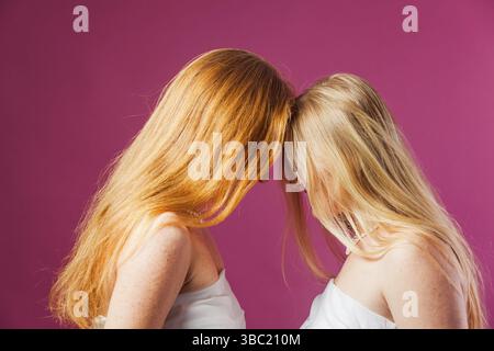 Portrait de deux jeunes femmes se tenant en face l'une de l'autre en touchant leurs fronts. Blonde et les femmes roux près l'une de l'autre avec les cheveux couvrant fac Banque D'Images