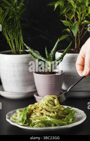 Pâtes avec arugula et pesto sur l'assiette. La main de la femme tient la fourchette avec des tagliatelles aux épinards Banque D'Images