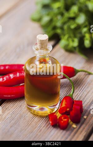 Le verre d'huile essentielle et tranches de piments sur une table en bois de gros plan Banque D'Images