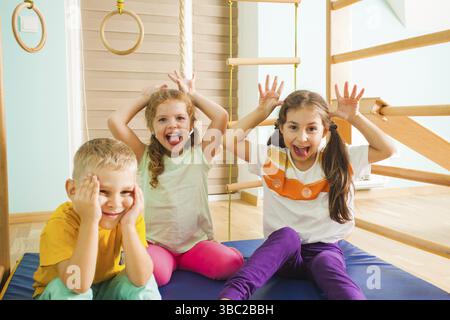 Portrait of smiling children on mate, regardant la caméra. Deux adorables filles et cute boy smiling, escalade sur les barres de bois Banque D'Images