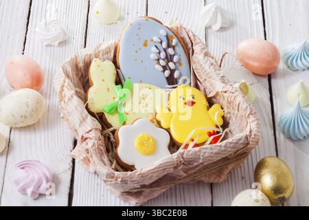 Le pain d'épice brillant en forme d'oeufs et de poulet se trouve dans un panier. À côté de sont des œufs peints sur la table Banque D'Images