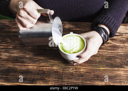 Processus de versement du lait dans le gobelet à thé matcha pour préparer l'art du Latte Fermez les mains Banque D'Images