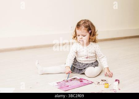 Fille, c'est peindre avec un pinceau et gouache sur papier sur le plancher Banque D'Images