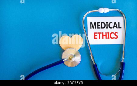 Symbole d'éthique médicale. Mots conceptuels éthique médicale sur une belle carte blanche. Coeur en bois et stéthoscope. Beau fond bleu. Médical sain Banque D'Images