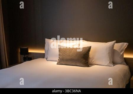 Un lit d'hôtel soigneusement fait avec des oreillers moelleux avec une lumière de lecture chaude Banque D'Images