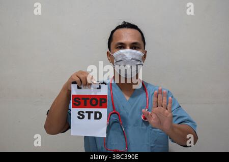 Jeune homme médecin montrant un geste d'arrêt et tenant du papier avec le texte Stop STD Banque D'Images