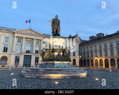 Statue en bronze de Jean-Baptiste Colbert se dresse sur une place de Reims, illuminée par de douces lumières sur fond de ciel nocturne. Banque D'Images