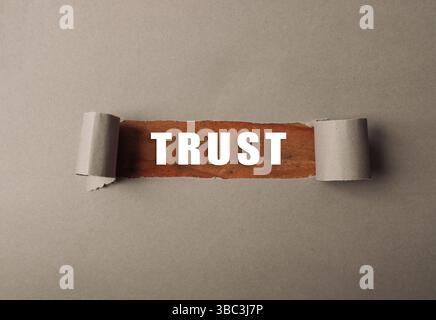 Morceau de papier déchiré avec le mot confiance écrit dessus. Le papier est brun et a un lettrage blanc Banque D'Images