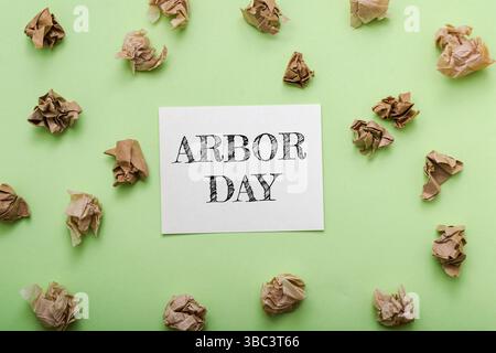 Panneau qui dit Arbor Day est sur un fond vert. Il y a beaucoup de morceaux de papier dispersés autour du panneau Banque D'Images