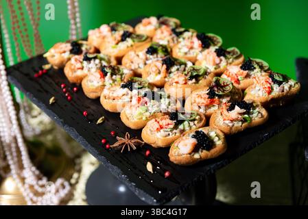 Canapés de fruits de mer élégants garnis de crevettes, de caviar, d'herbes et d'un mélange de salade, magnifiquement disposés sur un plateau de service sombre. Banque D'Images
