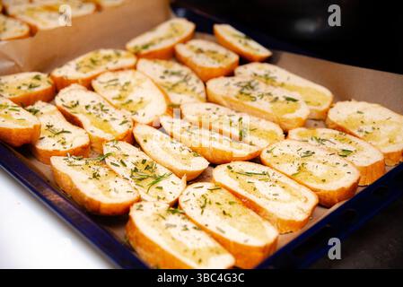 Gros plan de tranches de baguette fraîche garnies d'huile d'olive et d'herbes, disposées sur du parchemin pour griller ou préparer la cuisson. Banque D'Images