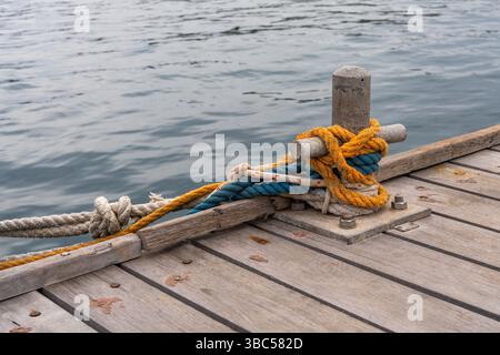 Gros plan de la borne d'amarrage avec des cordes multicolores vibrantes fixées autour, positionnées sur un quai en bois. Mer calme visible en arrière-plan. Nautique de Banque D'Images