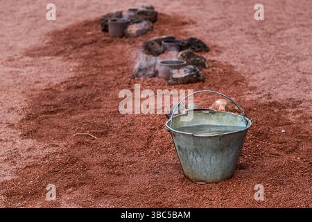 Des tuyaux enfoncés dans la cendre volcanique rouge de Lanzarote forment un geyser artificiel. L'eau versée s'évapore sur la couche de roche chaude en dessous et jaillit vers le haut sous forme de jet de vapeur. La démonstration se trouve à Islote de Hilario dans le parc national de Timanfaya. Banque D'Images