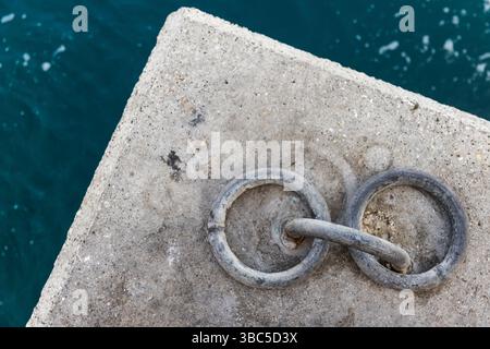 Une vue détaillée de deux anneaux d'amarrage interconnectés encastrés dans une surface de béton près d'une eau bleue calme Banque D'Images