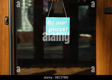Affiche « soyez notre client » accrochée à la porte vitrée à l'extérieur Banque D'Images