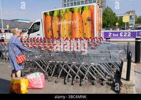 Une cliente ramène son chariot au rack derrière un van de marque Sainsbury garé, avec ses sacs à provisions placés sur le sol, par une journée ensoleillée à Londres Banque D'Images