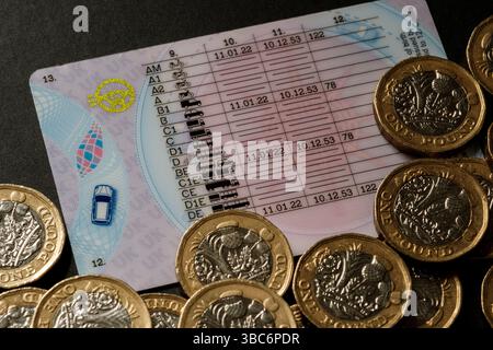 Gros plan du permis de conduire britannique montrant les catégories de véhicules et les dates d'émission, entouré de pièces britanniques d'une livre sur une surface sombre, Stafford, United Kin Banque D'Images