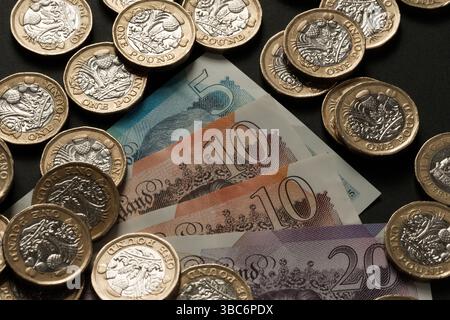 Billets de banque britanniques et pièces d'une livre dispersés sur une surface sombre, représentant la monnaie britannique, les flux de trésorerie et la richesse financière, Stafford, Royaume-Uni Banque D'Images