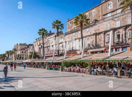 Split Riva, le front de mer de Split, en Croatie, qui s'étend le long de la mer Adriatique, avec des palmiers balançant, des cafés sur les trottoirs et une architecture historique Banque D'Images