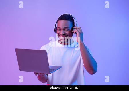 Black Gamer Man in Headset jouer à des jeux vidéo sur ordinateur portable, Neon Lighting Banque D'Images