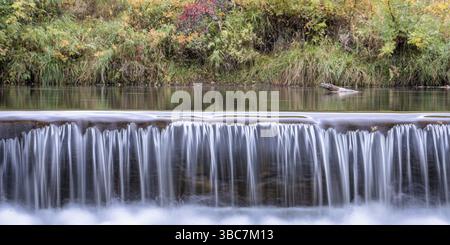 Au cours d'une cascade d'eau sur le barrage de dérivation du fleuve avec poudre de couleur à l'automne en arrière-plan, panorama Banque D'Images