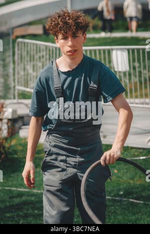 jeune jardinier avec un tuyau dans la main marche sur l'herbe Banque D'Images