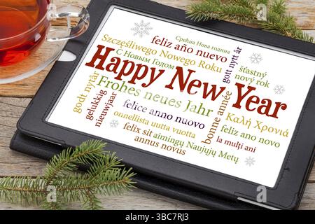 Bonne année dans différentes langues sur une tablette numérique avec une tasse de thé et des brindilles d'épinette Banque D'Images