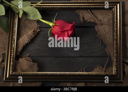 Dans un beau cadre, des morceaux de toile et une rose rouge sur fond de bois Banque D'Images