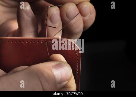 Fabrication de portefeuilles en cuir. Les mains du maître cousent un produit en cuir Banque D'Images