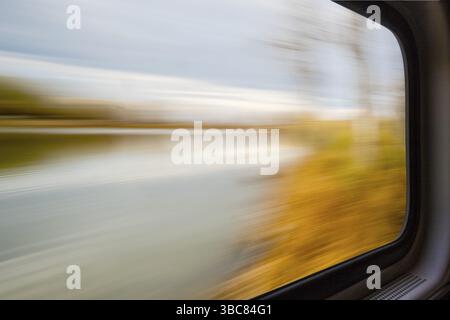 Paysage abstrait flou de lac et de forêt vu d'une fenêtre de train en mouvement Banque D'Images