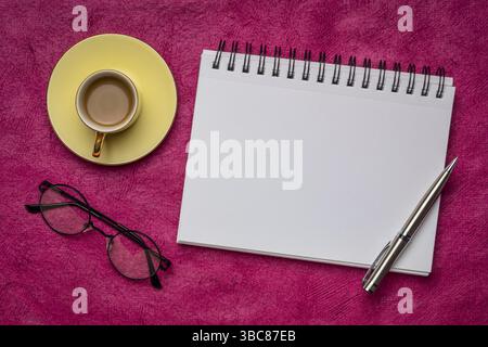 Carnet de croquis d'art en spirale vierge avec un stylo, des lunettes de lecture et une tasse de café contre du papier d'écorce texturée, espace de travail plat Banque D'Images