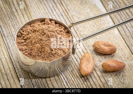 Poudre de cacao dans une cuillère à mesurer en métal contre fond de bois grunge avec quelques haricots crus Banque D'Images
