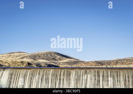 Eau en cascade au-dessus d'un barrage dans les contreforts du Colorado contre le ciel bleu Banque D'Images