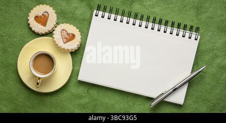 Carnet de croquis d'art en spirale vierge contre le papier d'écorce vert texturé, pose plate avec des biscuits au café et au cœur, concept de carte de voeux d'amour ou de romance Banque D'Images