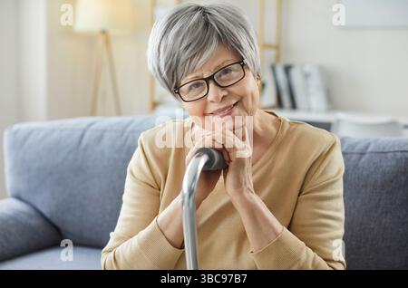 Portrait de femme aux cheveux gris heureux posant avec un bâton de marche, concentré à la caméra et souriant Banque D'Images