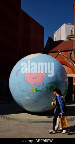 Un Hugh Globe de la planète Terre dans une rue étroite avec des jeunes marchant devant dans la ville de Londres, en Angleterre Banque D'Images