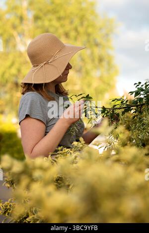 Femme dans un chapeau de paille touchant une branche d'arbre dans le jardin. Banque D'Images