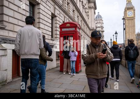 Touriste prenant une photo avec son smartphone avec une cabine téléphonique rouge emblématique à la périphérie du Palais de Westminster avec Big Ben dans la ville Banque D'Images