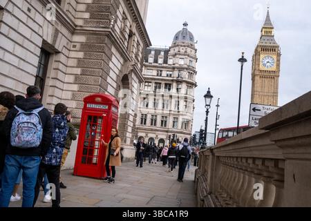 Touriste prenant une photo avec son smartphone avec une cabine téléphonique rouge emblématique à la périphérie du Palais de Westminster avec Big Ben dans la ville Banque D'Images